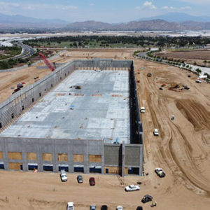 Aerial view of large concrete building construction site with heavy machinery and mountain backdrop.