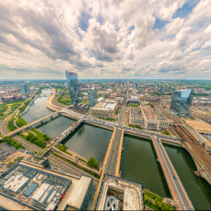 Modern urban skyline with skyscrapers, waterways, construction cranes, and dramatic cloudy sky.