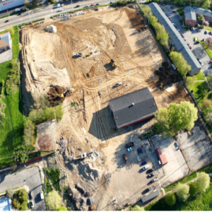 Aerial view of construction site with excavation, grading equipment, and surrounding urban development.
