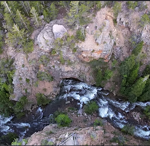 Aerial view of rushing river through rugged forest canyon and rocky cliffs.
