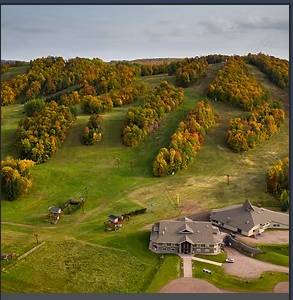 Autumn foliage surrounds a mountain resort lodge with ski lifts on rolling hills.