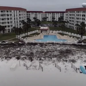 Beachfront condo resort with pool, white sand beach, palm trees, and ocean views.