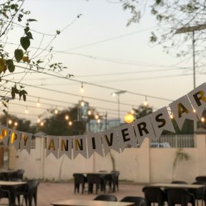 Happy Anniversary banner over outdoor patio tables with string lights.