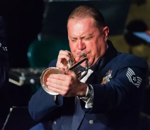 Military trumpet player performs passionately on stage in uniform.