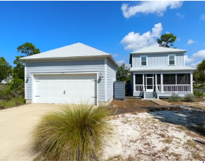 Modern coastal home with detached garage, porch, driveway, and pine trees.