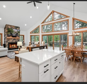 Open concept living room with stone fireplace, kitchen island, dining area, and large windows.