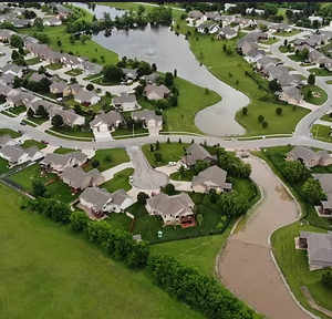 Aerial view of suburban neighborhood with pond, homes, winding streets, and green spaces.