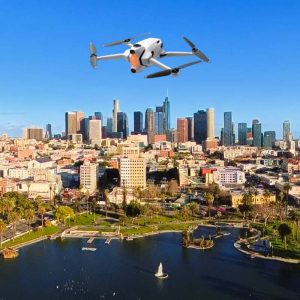 Drone captures aerial waterfront city skyline with sailboat, parks, and blue sky.