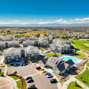 Drone view of modern apartment complex with pool, parking, landscaping, and mountain views.
