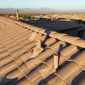 Terracotta roof tiles with chimneys overlooking desert mountains at sunset.
